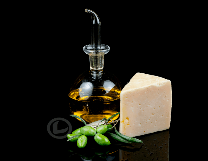 Cuña de queso en aceite Mozalba al lado de una aceitera con AOVE y una rama de olivo con aceitunas verdes