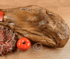 jamón ibérico entero de Vuelta y Vuelta. En la imagen también se ve un plato con el jamón ya cortado y un tomate