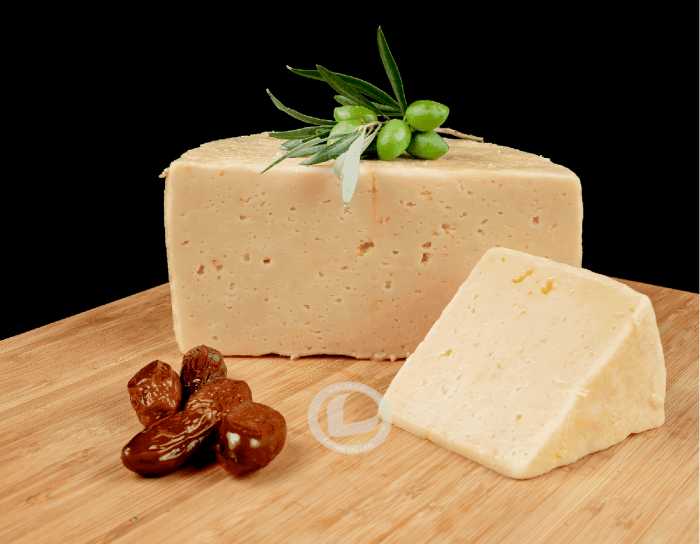 Queso en aceite la mozalba, medio queso y una cuña. Delante dátiles y una rama de olivo con aceitunas verdes