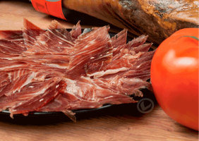 plato de jamón ibérico cortado de Vuelta y Vuelta. También aparece un tomate en primer plano