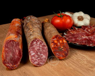 pack ibérico Vuelta y Vuelta: lomo, salchichón y chorizo, y un plato de jamón cortado. También aparece un ajo y un tomate.