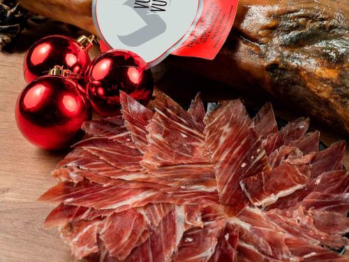 Un plato con jamón ibérico cortado, al lado un jamón entero y tres bolas de navidad