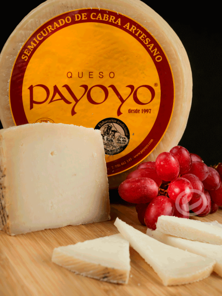 Queso payoyo semicurado de cabra, uno entero, una cuña y varios cortes. También un racimo de uvas negras