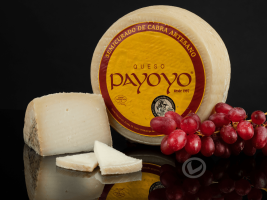 Queso payoyo entero y delante una cuña y varias lonchas. También aparece un racimo de uvas negras.