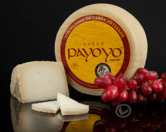 Queso payoyo entero y delante una cuña y varias lonchas. También aparece un racimo de uvas negras.