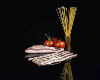 Trozo de guanciale, lonchas cortadas, tres tomates y un recipiente con spaguettis